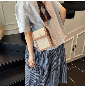Detail of canvas crossbody phone bag with brown leather trim and clover metal clasp