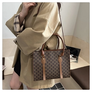 Detail of a brown structured crossbody bag with M-pattern print on a model