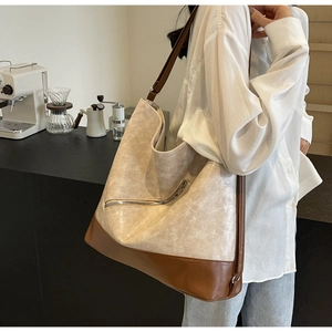 Detail of beige and brown leather tote bag with metal zipper worn by a model