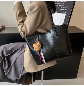 Detail of black large capacity tote bag with bear charm and woven straps on model