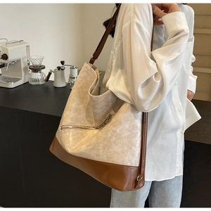 Close-up of large tote bag featuring cream pebbled leather and brown trim on a model