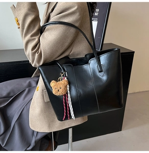 Macro shot of black faux leather tote bag texture with cute bear charm and woven detail