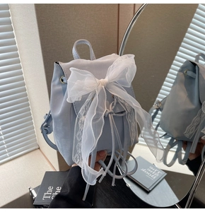 Detail of light blue mini backpack with large white lace bow and drawstring closure