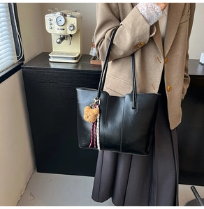 Detail of black glossy PU leather tote bag featuring a cute brown plush bear charm