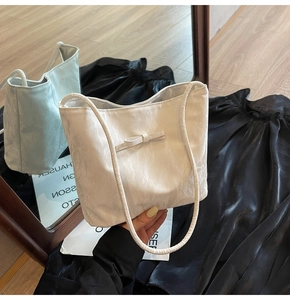 Détail du sac seau en cuir plissé blanc avec un nœud minimaliste et des poignées fines