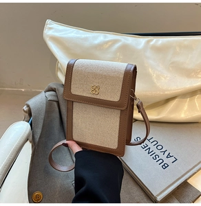 Detail of canvas crossbody bag with brown leather trim and golden clover ornament