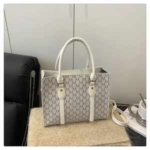 Detail of white PU leather tote with gray M pattern and gold hardware on plush mat