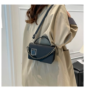 Detail of black crossbody bag featuring a unique square metal logo and woven chain strap
