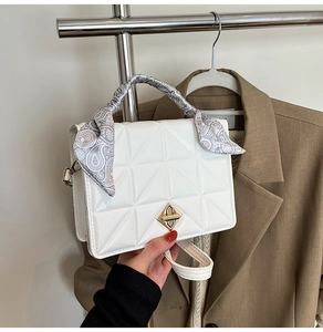 Détail d'un sac à main blanc matelassé avec fermoir doré et poignée ornée d'un foulard