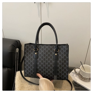 Detail of black tote bag featuring M-letter jacquard pattern and gold hardware accents
