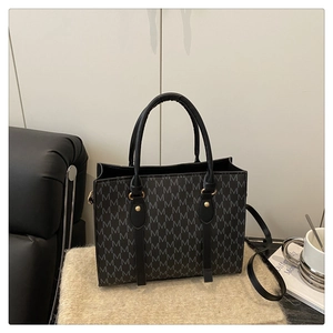 Detail of grey M-letter monogram tote bag with gold hardware on a beige plush rug