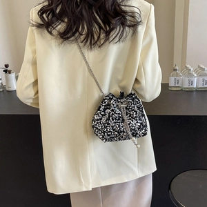 Silver sequin drawstring bucket bag with chain strap worn by model on shoulder