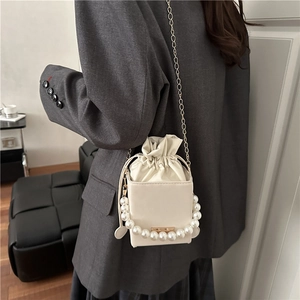 Elegante cremefarbene Eimertasche mit Perlen Griff und Goldkette als Schultertasche