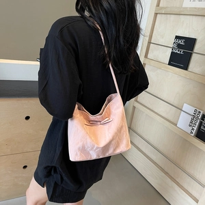 Sac hobo rose plissé avec nœud décoratif, porté à l'épaule dans un intérieur chic