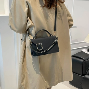 Chic black minimalist leather crossbody bag with gold buckle on trench coat model