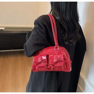Detail of red glossy patent leather shoulder bag featuring decorative ribbon bows