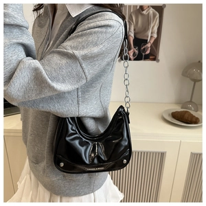 Detail of black glossy half-moon shoulder bag with silver rivets and metal chain strap