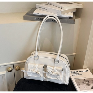 Détail du sac à main blanc en cuir avec nœuds et poches avant sur une surface texturée