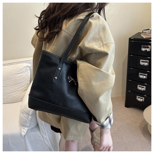 Detail of black PU leather tote bag with gold bow ornament and metal rivets on model
