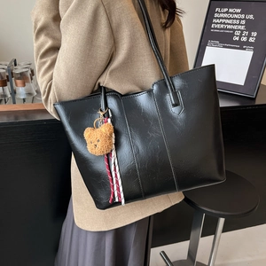 Minimalist black PU leather tote bag with plush bear charm in a cafe setting