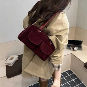 Chic burgundy suede shoulder bag with twin front pockets worn by a model in a warm room