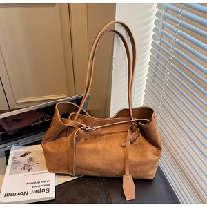 Close-up of caramel suede tote bag with slim straps on a desk in a warm urban office