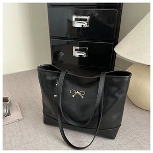 Detail der schwarzen Shopper-Tasche mit goldener Schleifenschnalle und Lederstruktur