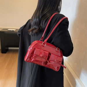 Sac Boston en cuir verni rouge avec nœuds porté par un mannequin en blazer noir