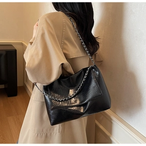 Detail of black glossy crinkled leather shoulder bag with silver metal chain strap