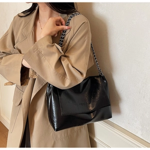 Close-up of black glossy leather tote bag with silver chain strap on khaki trench coat