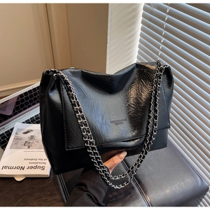 Detail of black glossy pleated tote bag with silver double chain straps and embossed logo