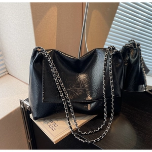 Close-up of black glossy chain shoulder bag featuring crinkled leather and silver hardware