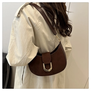Dettaglio borsa a mezzaluna in camoscio marrone con fibbia dorata su cappotto beige