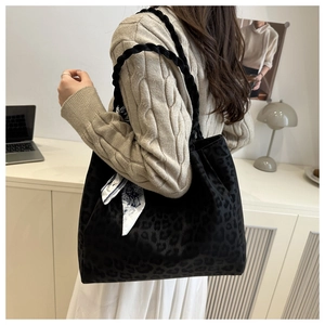 Detail of black leopard print tote bag with woven straps and decorative white scarf