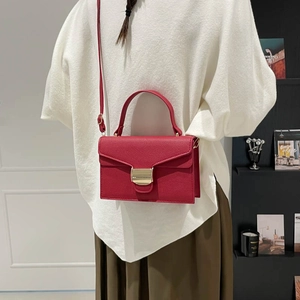 Sac à main chic en cuir rouge à boucle dorée, porté par un mannequin dans un cadre élégant