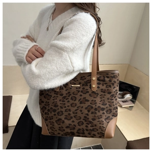 Detailed view of leopard print tote bag with brown leather straps and gold metal logo bar