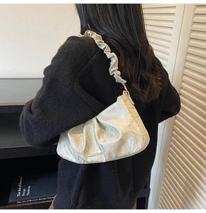 Close-up of light green pleated shoulder bag with ruffled strap and metal logo