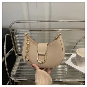 Dettaglio borsa a mezzaluna beige con catena dorata e chiusura in metallo a forma di U
