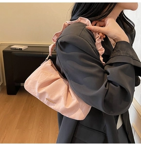 Pink pleated shoulder bag with ruffle strap and golden logo detail on a model