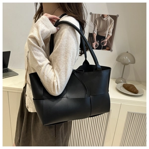 Close-up of black woven leather tote bag shown on model for shoulder wear
