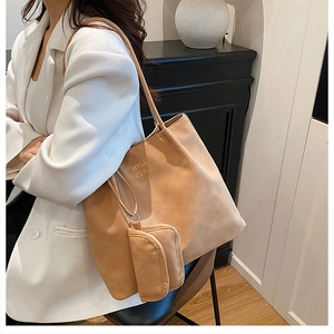 Detail of camel tote bag with HYLL ZZA logo and matching small pouch in a home setting