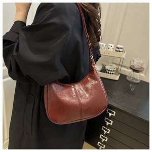 Detail of burgundy glossy pleated crescent bag worn with a black coat in a cozy room