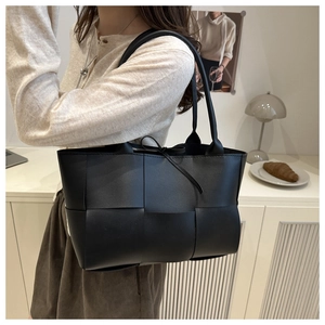 Close-up of black woven leather tote bag featuring large weave detail and strap knot