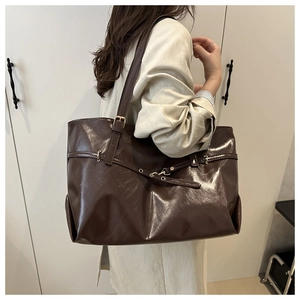 Close-up of a large brown patent leather tote bag with strap buckle details on shoulder