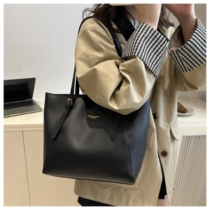 Detail of a black large-capacity tote bag with a golden metal logo plaque and sleek straps