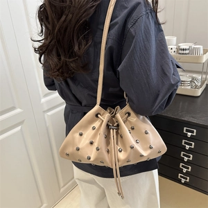 Beige bucket bag with studs and drawstring closure shown on shoulder for casual style
