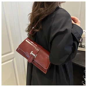 Detail of burgundy leather underarm bag with silver H-buckle worn by a model