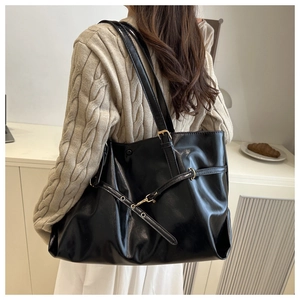 Side view of a large black glossy tote bag with metal buckle strap worn by a model