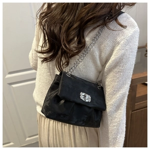 Detail of a black textured crossbody bag with silver chain strap and crystal square buckle