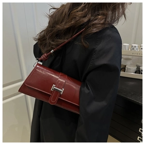 Détail du sac baguette en similicuir rouge foncé avec boucle argentée et nœud sur la sangle